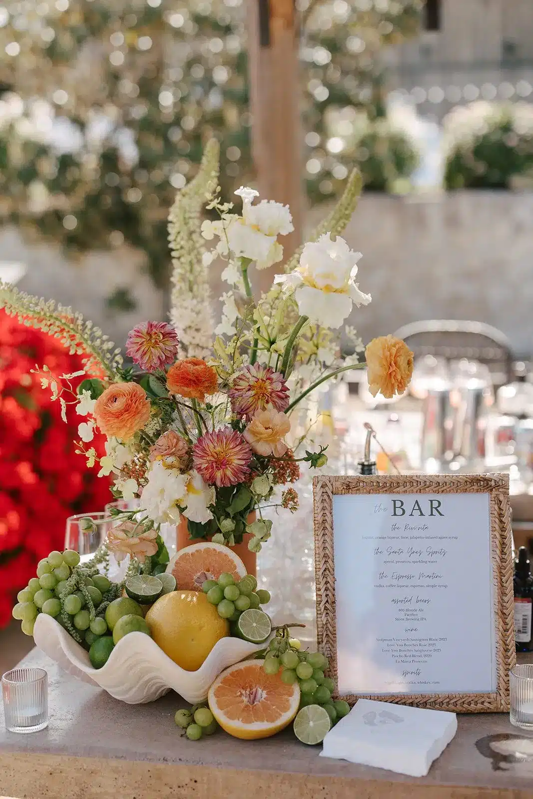 Floral arrangement with citrus fruits, including lemons, limes, and oranges, alongside a decorative bar menu sign, enhancing a stylish beverage station for events.
