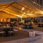 a sleek, modern corporate event setup featuring an elegantly arranged tent with sophisticated seating, polished table settings, and ambient lighting, all set against a bustling urban backdrop that embodies professionalism and style.