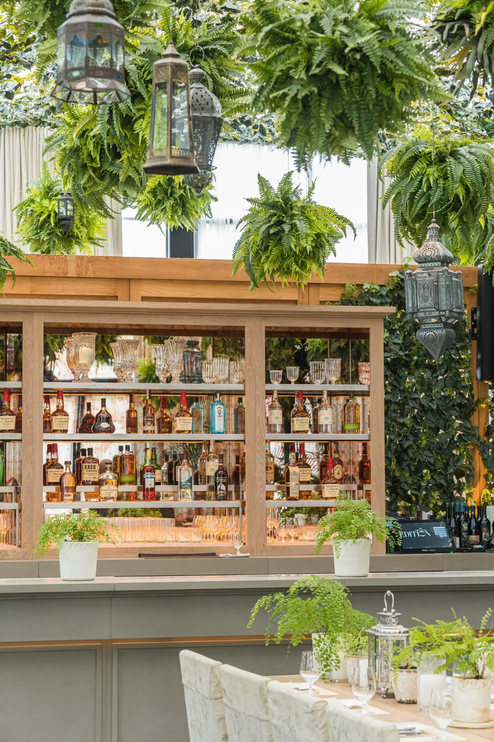 Stylish portable bar setup featuring a well-stocked shelf of liquor bottles, elegant glassware, and decorative greenery, ideal for enhancing event experiences with Ventura Rentals.
