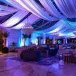 a sophisticated indoor event space, seamlessly designed with elegant tents and versatile decor, showcases a polished setting ready to accommodate guests under any weather condition, illuminated by vibrant, adjustable lighting.