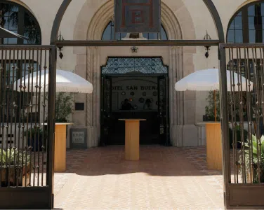 Entrance of Hotel Kan Buen with wooden tables and white umbrellas, showcasing a welcoming atmosphere and architectural details.