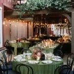 Elegant holiday dinner setup with green table linens, candlelight, and warm string lighting.