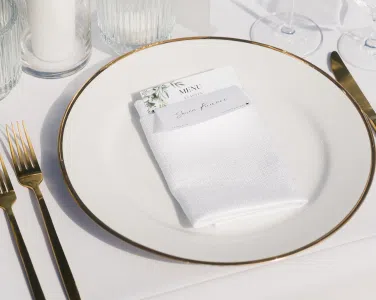 Elegant white plate with gold rim, neatly arranged napkin and menu card, brushed gold flatware, and glassware, showcasing a refined dining setting for weddings at Tuscan Hills Estate.
