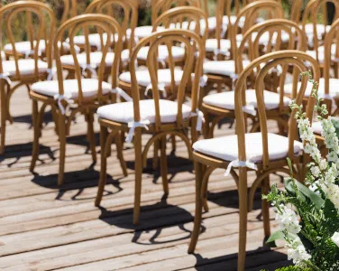 Bentwood Natural Chairs arranged for an outdoor wedding ceremony at Tuscan Hills Estate, featuring natural wood finish and white cushions, set against a rustic wooden deck and greenery.