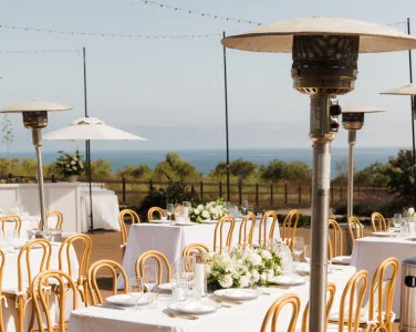 Outdoor dining setup with Silver Patio Heaters and elegant table settings, featuring white tablecloths and floral centerpieces, overlooking a scenic view at Tuscan Hills Estate.