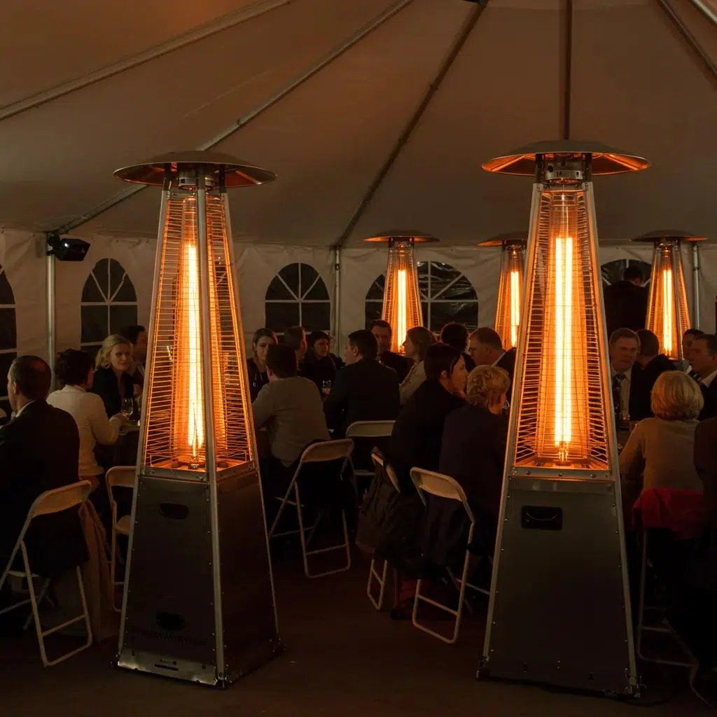 Interior of a tent featuring radiant heaters providing warmth during a winter event, with guests seated around tables in a cozy atmosphere.