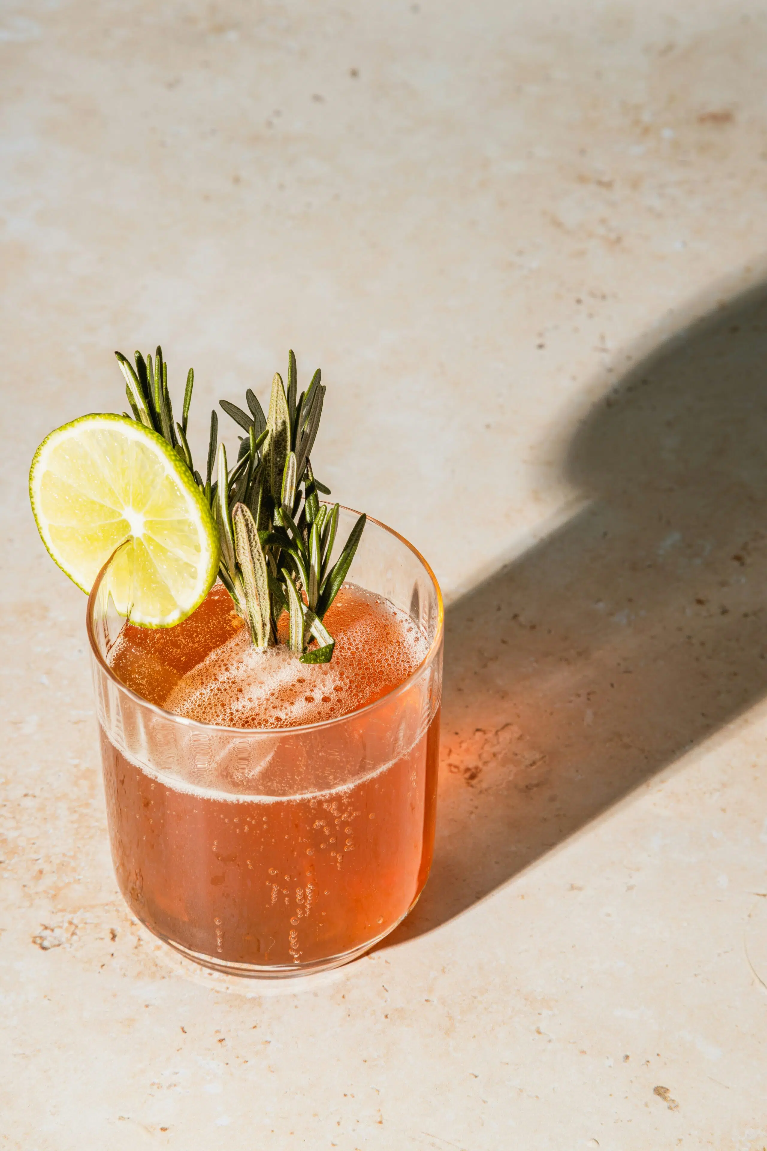 Elegant cocktail featuring a rosemary garnish and lime slice, set against a textured surface, ideal for a Christmas cocktail party in Ventura.