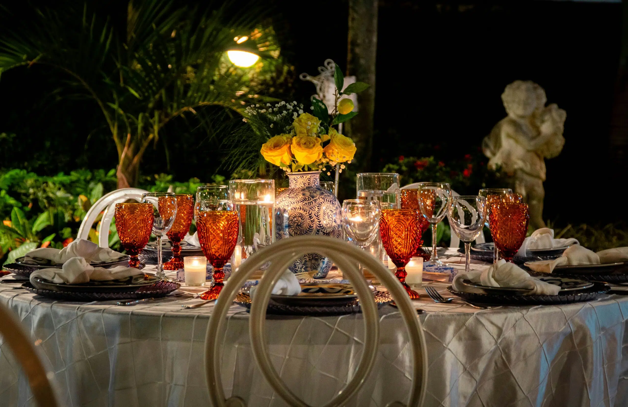 Elegant coastal dining table set for winter gatherings featuring amber glassware, blue and white vase with yellow roses, candlelight, and natural greenery backdrop, embodying warmth and festive charm.