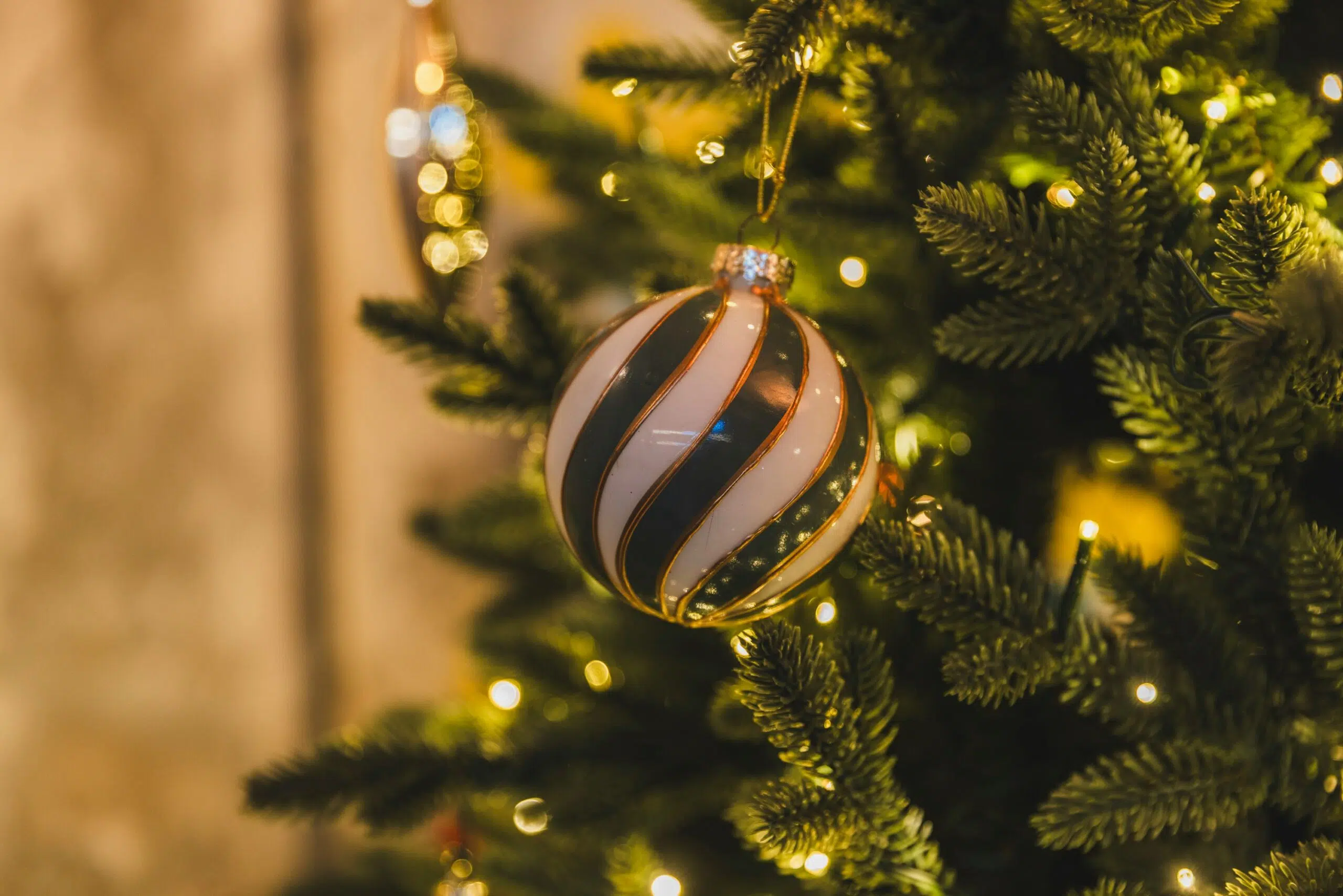 Christmas ornament with green and white stripes hanging on a decorated tree, surrounded by warm lights, enhancing festive office decor for employee engagement.