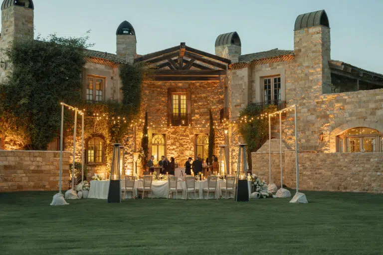 Elegant outdoor wedding reception at a rustic stone venue, featuring a beautifully set table, ambient lighting, and guests mingling in a lush garden setting.