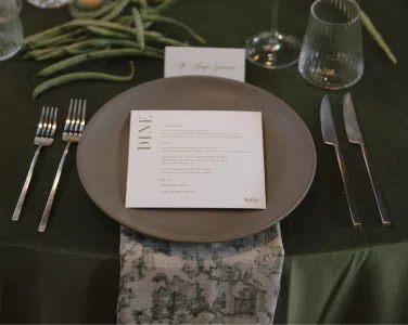 Elegant wedding table setting featuring a round olive shantung linen tablecloth, basic matte silver flatware, Verona ridged glassware, and a menu card, creating a romantic dining experience for guests at a Santa Barbara wedding.
