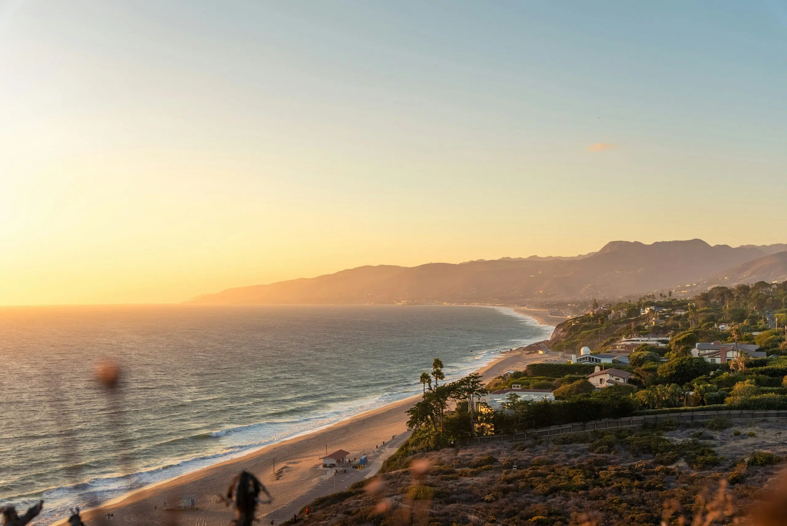 Coastal landscape of Malibu at sunset, featuring sandy beach, ocean waves, and hillside homes, illustrating the scenic backdrop for outdoor events and tent rentals.