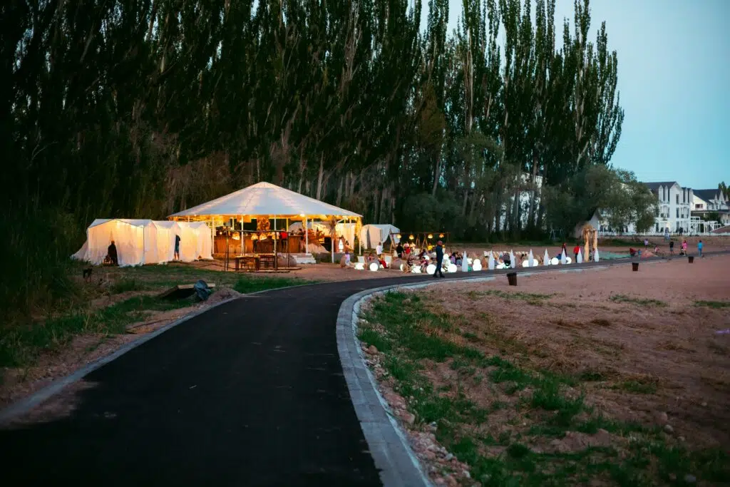 Outdoor event setup with a large white tent, illuminated decorations, and guests enjoying the gathering along a scenic pathway, reflecting Ventura Rentals' event planning services.