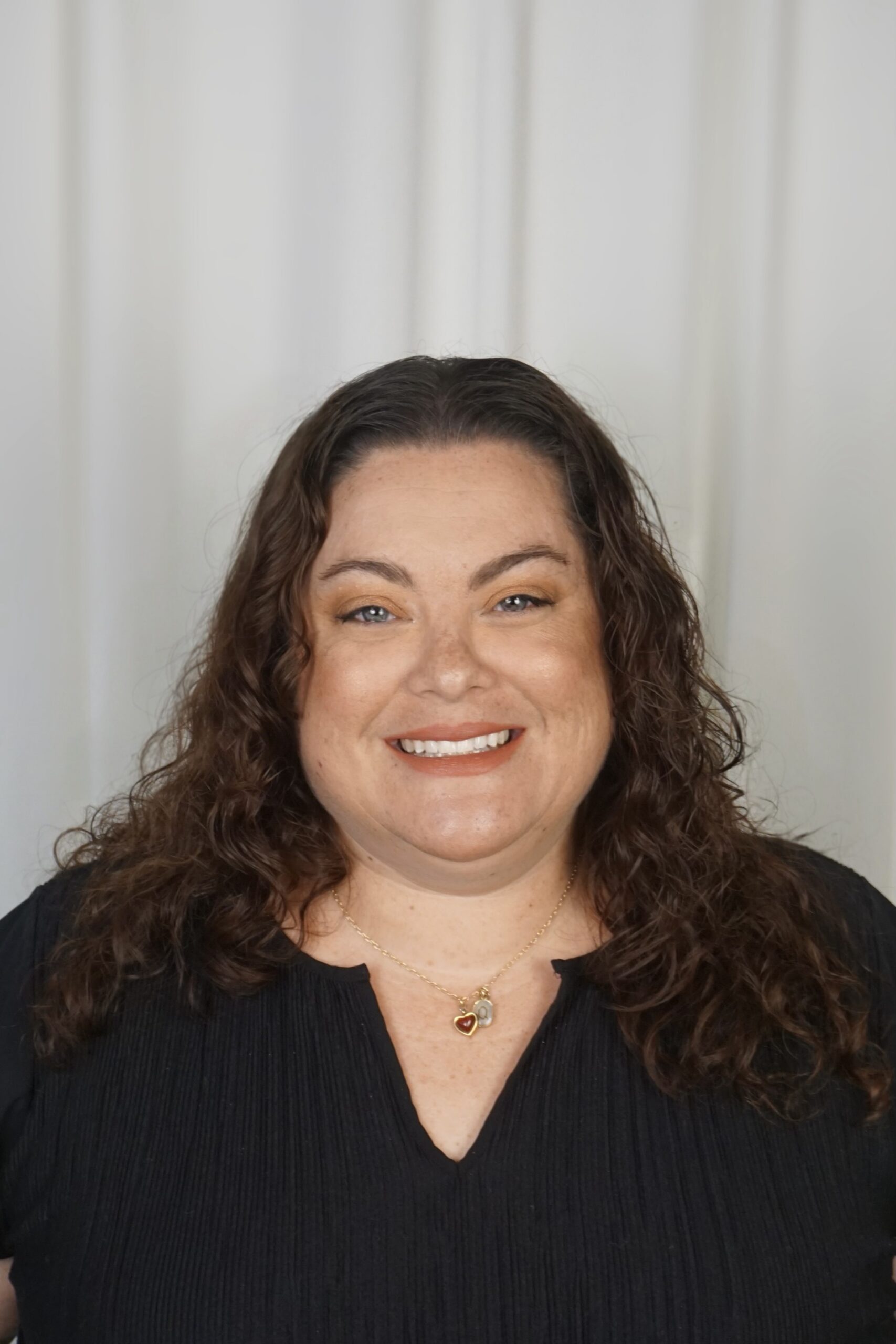 Smiling woman with curly hair wearing a black top and necklace, representing the team at Ventura Rentals.