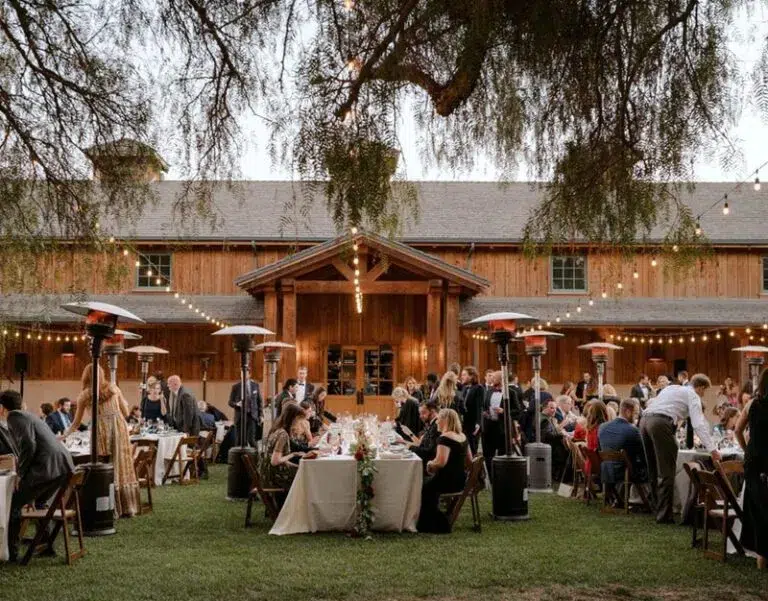 Outdoor dinner reception with dining tables, wood chairs, patio heaters, string lights, and a rustic wood venue.
