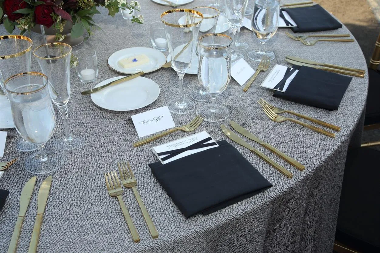 Gala sample table with textured linen, gold flatware, glassware, and black napkins