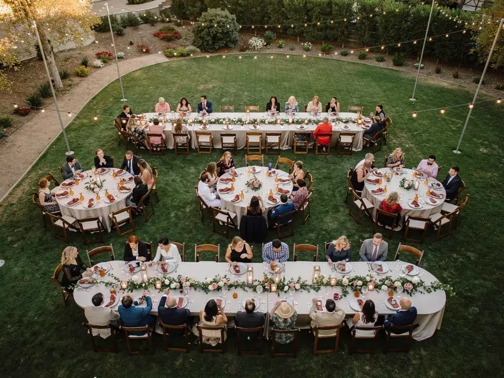 Aerial view of outdoor dinner tables with wood chairs arranged on a lawn for a fall gathering.