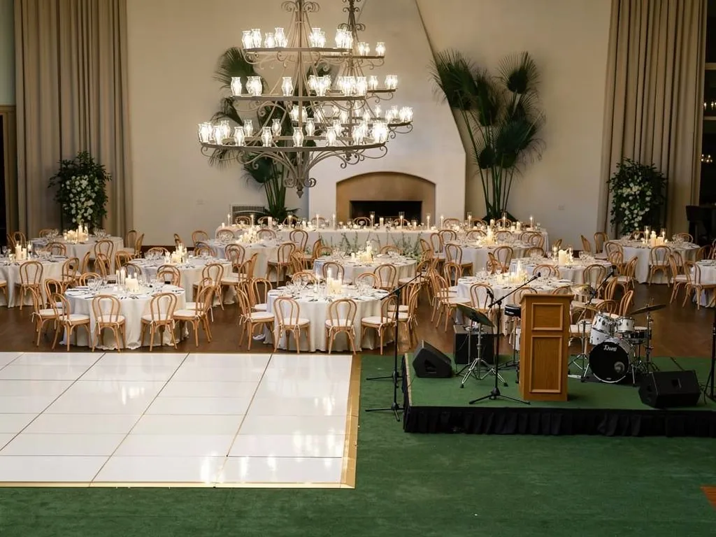 Indoor event setup with white dance floor, band stage, and surrounding dining tables