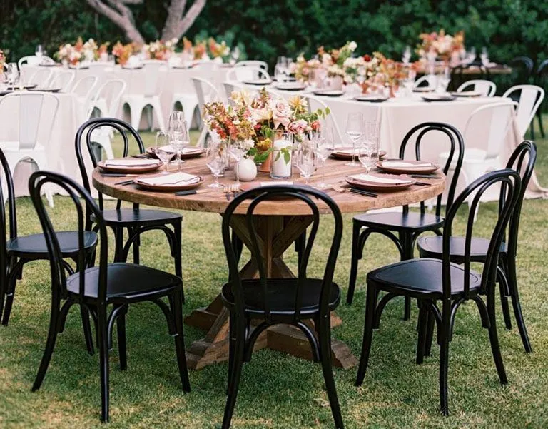 Elegant outdoor dining setup with round wooden tables, black chairs, and floral centerpieces