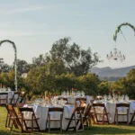 Elegant outdoor event setup with round tables, floral arches, and mountain backdrop