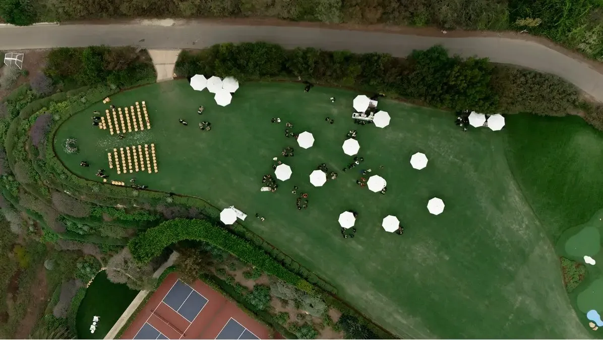 Outdoor event setup with chairs, umbrellas, and guests on green grass