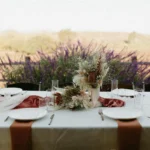 Elegant dining table with floral centerpiece and purple flowers in background